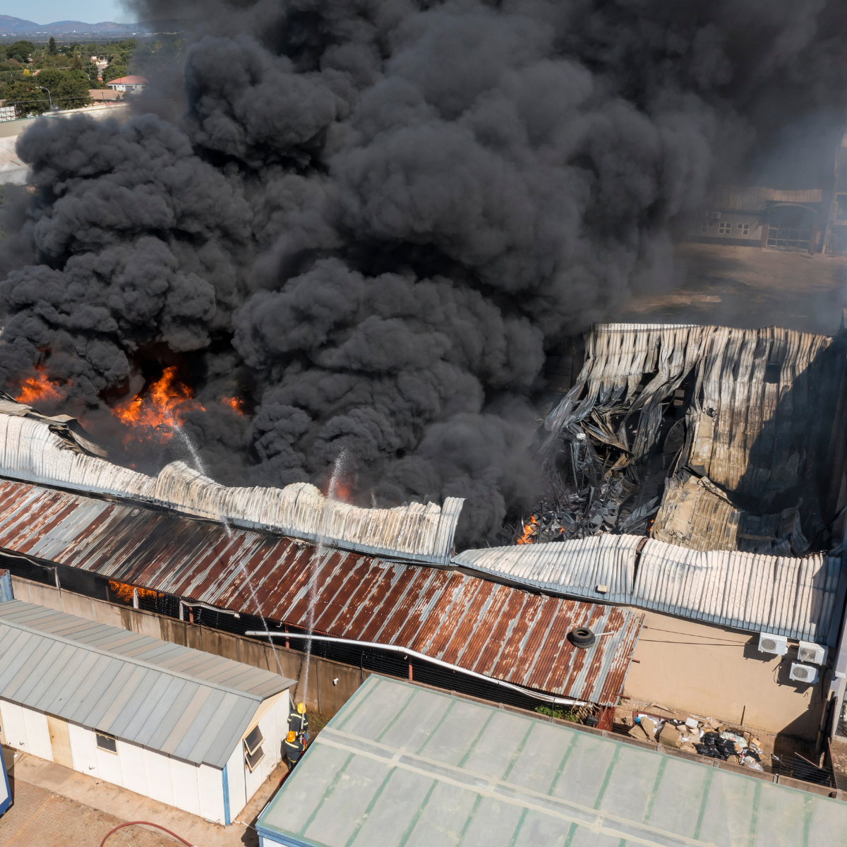 Image of a large warehouse on fire with black clouds of smoke using an aerial view